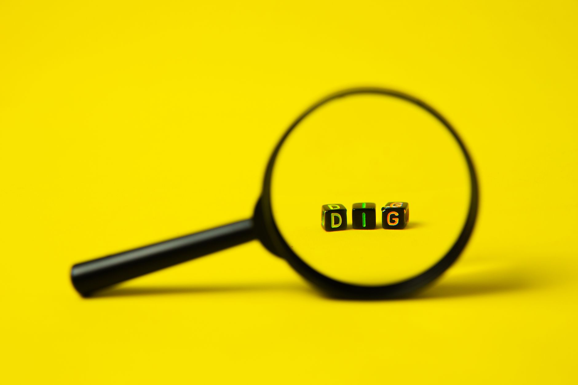 Background of big black magnifier with word dig in form of cubes against yellow surface
