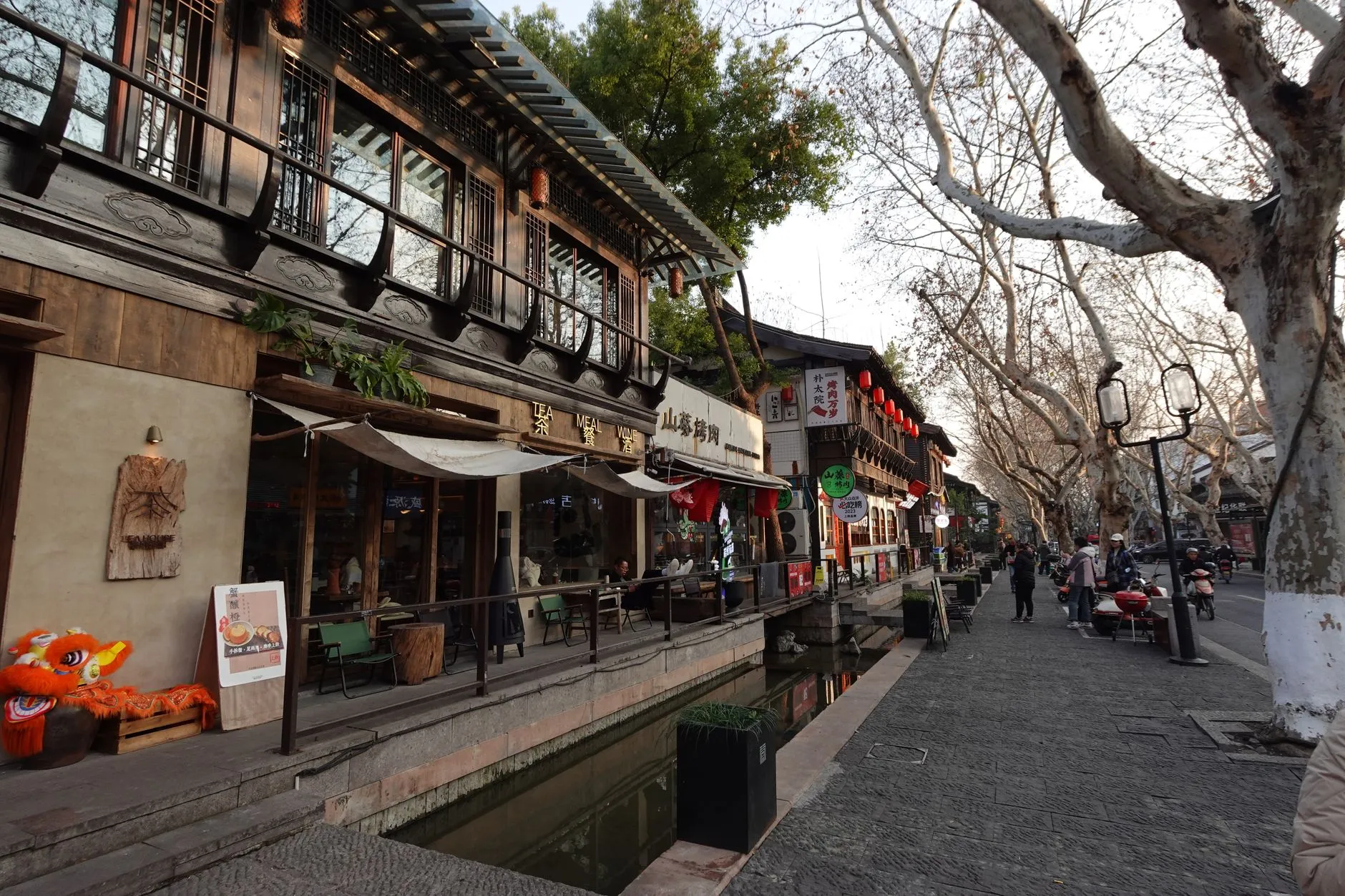 Bustling traditional street in Hangzhou, China, lined with shops and a scenic canal, capturing local culture and architecture.