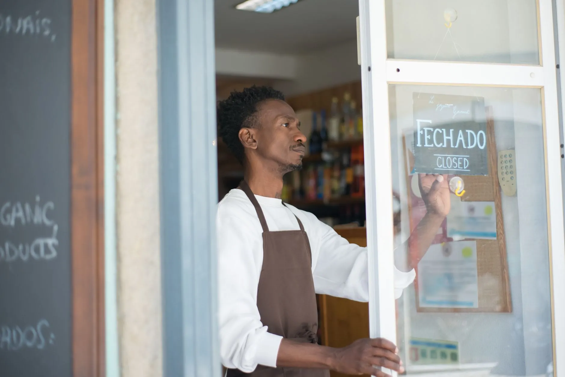 African man closing a store with a sign in Portuguese, wearing an apron.
