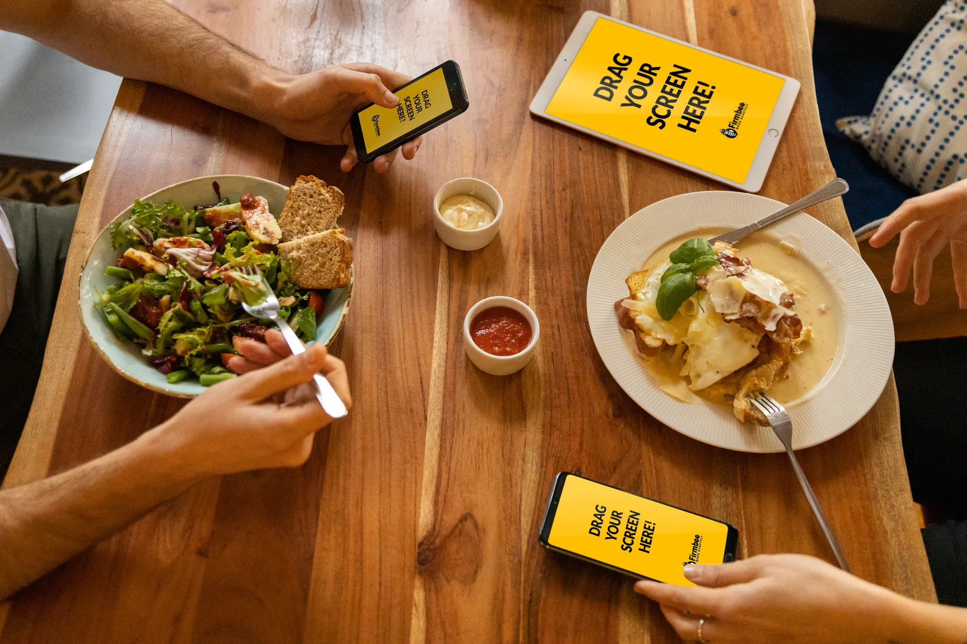 Group dining with electronic devices and fresh meals on a wooden table.
