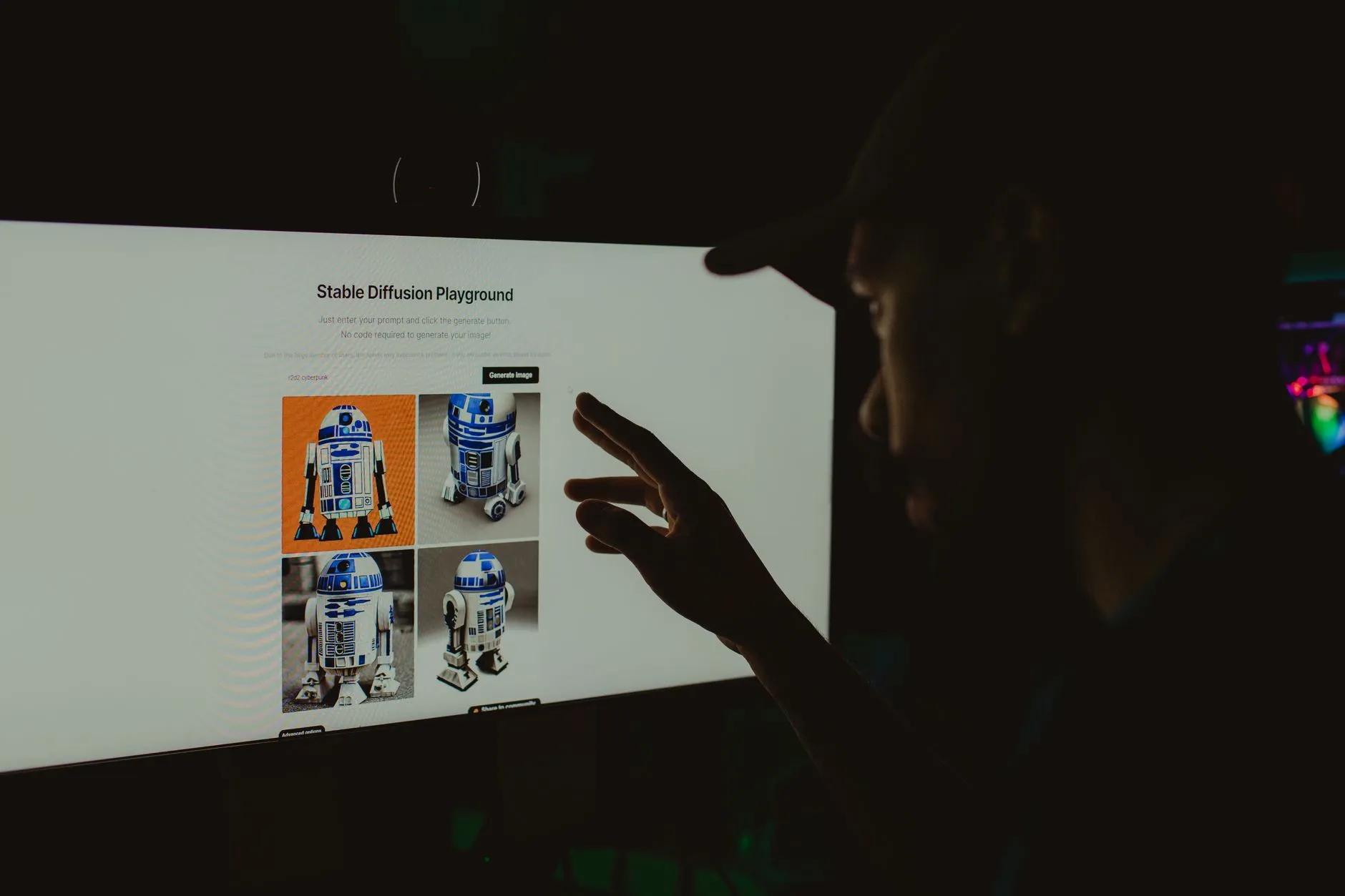 Person interacts with robot images on a screen in a dark room, highlighting technology use.