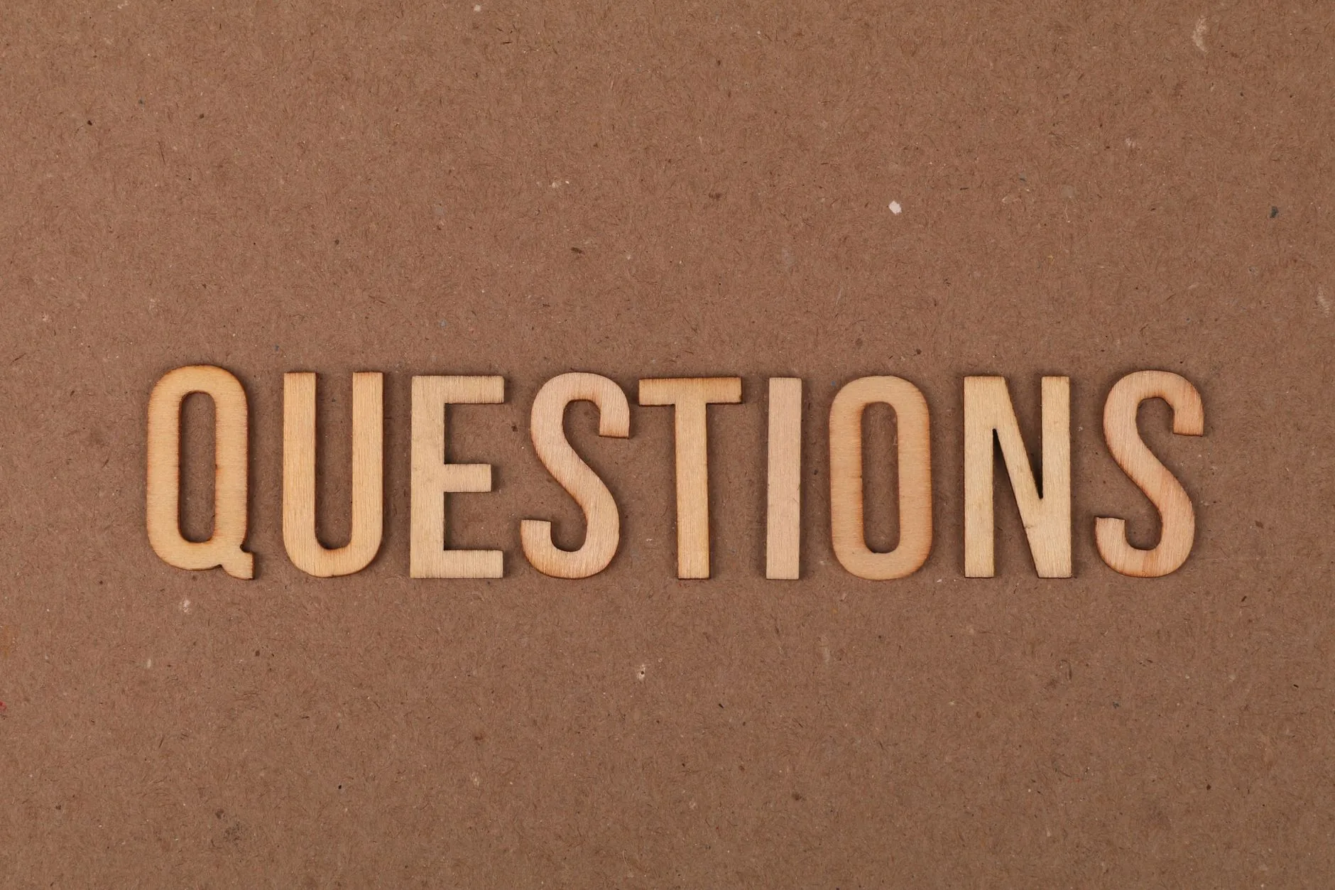 Wooden letters spelling the word "QUESTIONS" on a cardboard background, providing a neutral copyspace.