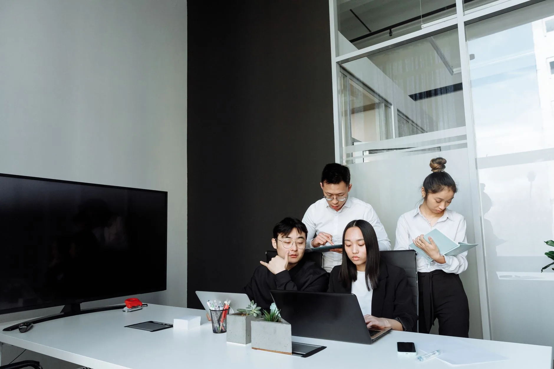 Team of young professionals collaborating in a modern office setting, engaging with laptops and documents.