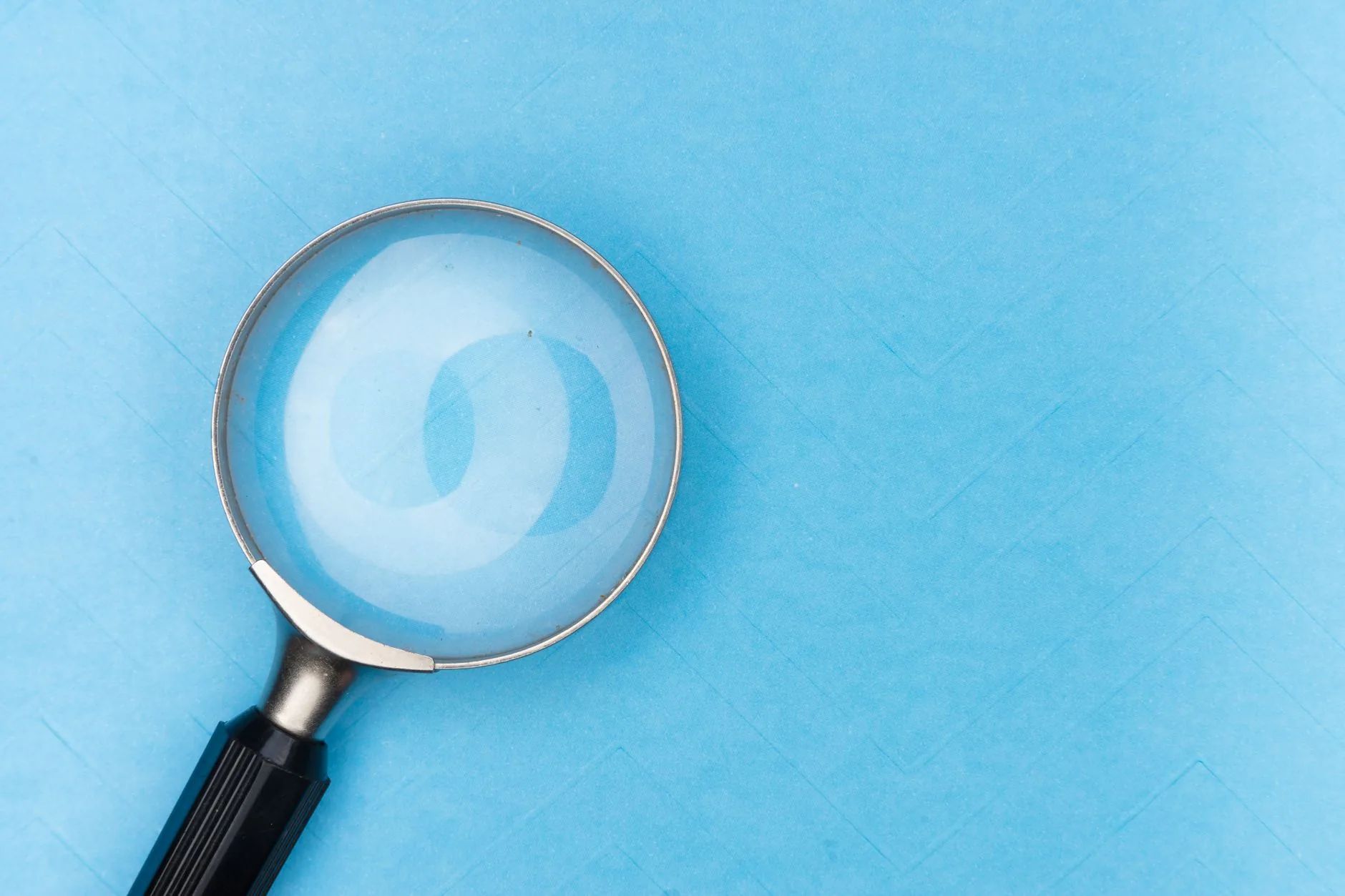 Close-up of a magnifying glass on a blue surface, ideal for search and exploration themes.